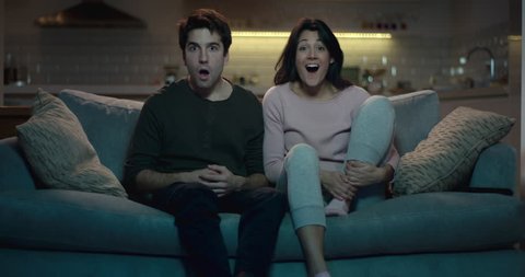 Man and woman watching tv with shocked expressions on their faces.