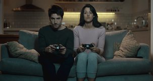 Competitive couple push and shove each other as they play a video game at home