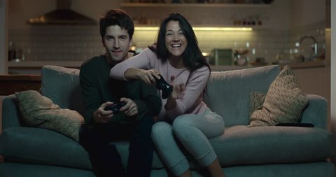 Competitive couple push and shove each other as they play a video game at home
