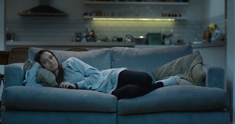 Young woman lying down on a comfy sofa at night watching the television Adlı Stok Video