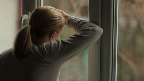 A crying woman is standing by the window