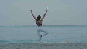 Beautiful young girl exercising in the morning on the sandy beach - video in slow motion