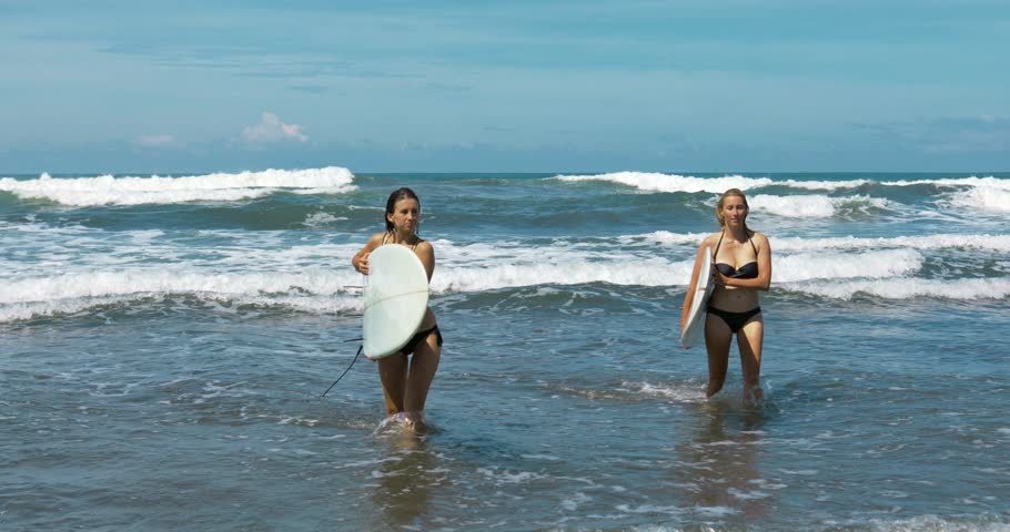 Two girls going out from the ocean with their surfboards. Shot taken by a handheld gimbal