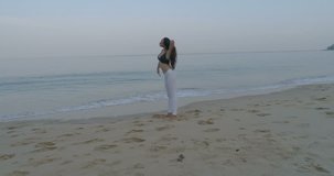 Aerial view of beautiful young girl exercising in the morning on the sandy beach - video in slow motion