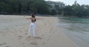 Aerial view of beautiful young girl exercising in the morning on the sandy beach - video in slow motion