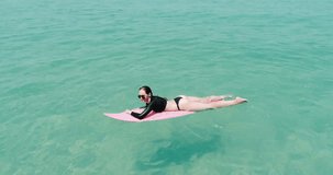 Aerial top view of beautiful young woman in swimsuit and sunglasses with pink surfboard enjoying her holiday in amazing clear sea water - video in slow motion