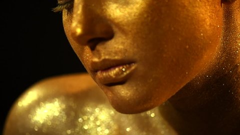 High Fashion model woman in golden bright sparkles posing in studio, portrait of beautiful sexy girl, trendy glowing gold skin make-up. Art design make up. Glitter metallic shine makeup 4K slow motion