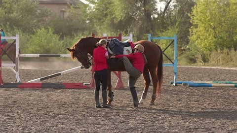 A female coach helps a child to climb a horse, learning to ride a horse at a horse farm. Children are engaged in horse riding. Slow motion.