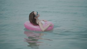 Beautiful young woman in swimsuit and sunglasses with pink inflatable ring having fun in the sea water, enjoying sunny summer day on her beach tropical holiday - video in slow motion