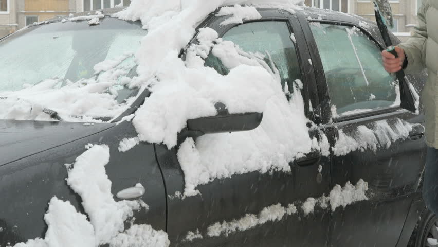 Caucasian man is cleaning black car from snow during snowfall in the yard