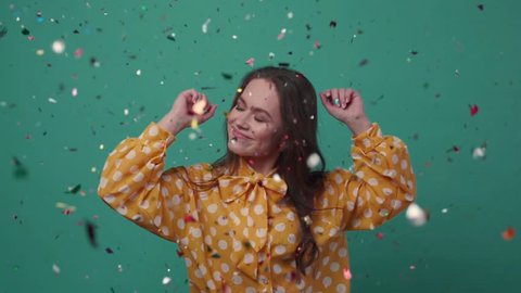 Beautiful young woman dances alone in colorful confetti on a green background. 
