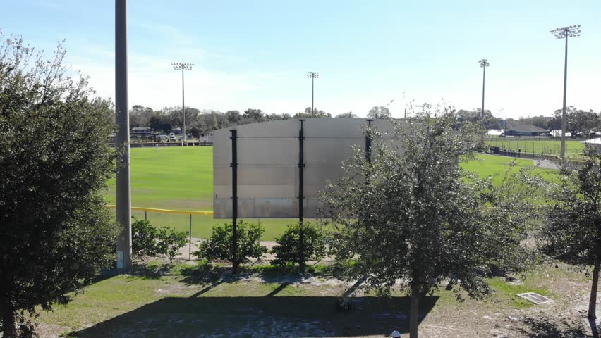 This shot continues to rise, and then pan down keep the game in focus after rising over the scoreboard, and then the lights, to reveal Florida Baseball and also a sparkling Lake in the background.