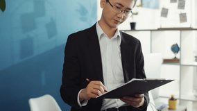 asian young businessman hold documents look at camera unhappy shrugs in office chinese japanese attractive handsome happy fashion men business leader businessperson company slow motion
