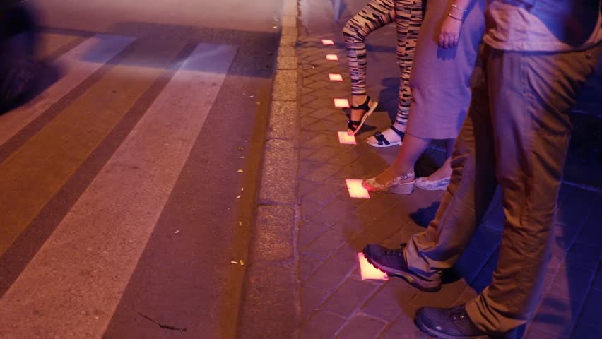 Legs of woman and two teenagers cross road at traffic light in asphalt in night