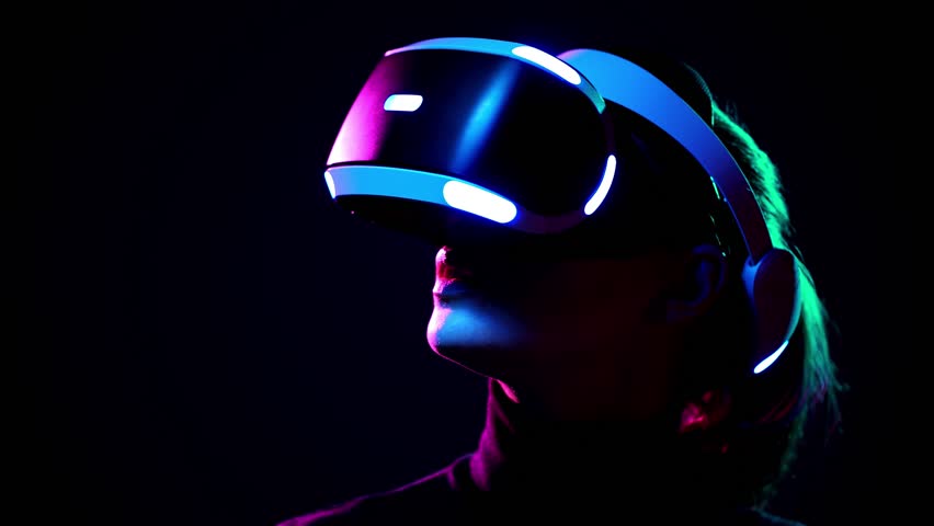 Young woman in VR headset looks around and wonders how amazing. Virtual reality helmet on black background