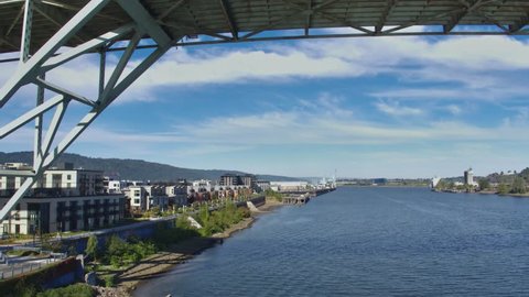 Aerial tracking shot, starting from under the bridge and moving towards the old morning dock, of riverside apartments and condos on a sunny day. : vidéo de stock