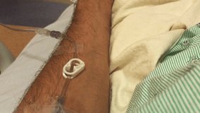 Close-up of man’s arms opening and closing hand while wearing an IV at hospital