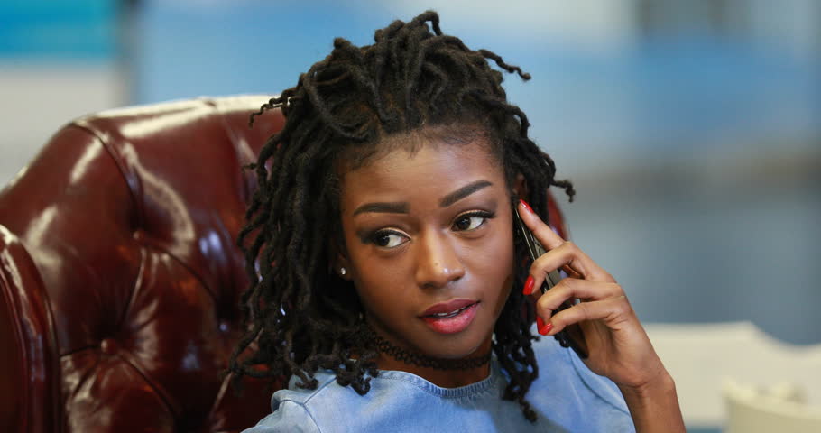 African American woman sitting and talking, Young black girl flirting on smartphone on brown armchair. 