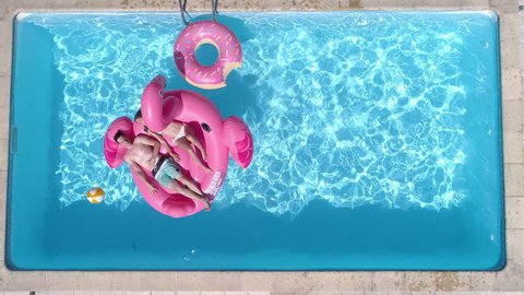 Aerial - Couple lying on a giant inflatable pink flamingo floatie in the pool at home