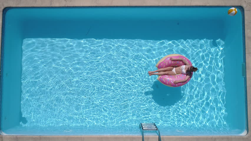 Aerial - Adult man dives into the the pool while girl is lying on a donut pool float (slow motion) | Shutterstock HD Video #1009227818