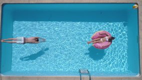 Aerial - Adult man dives into the the pool while girl is lying on a donut pool float (slow motion) - Powered by Shutterstock - Get 15% off with code: PIKWIZARD15