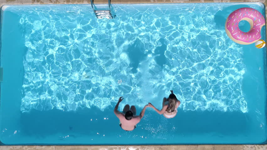 Aerial - Couple holding hands and jumping in the pool like a cannon ball at the same time. A fun summer day in the pool at home (slow motion) Royalty-Free Stock Footage #1009227836