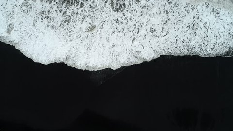 Aerial footage of waves breaking against black sand beach in Iceland.