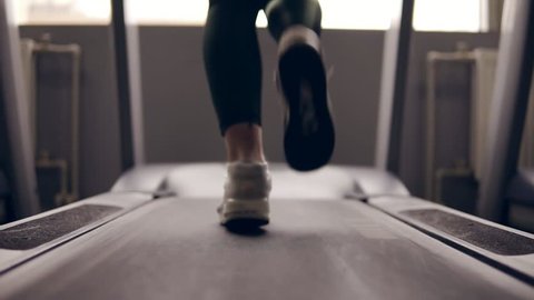 Slow motion footage of supposedly female legs in sneakers running on treadmill.