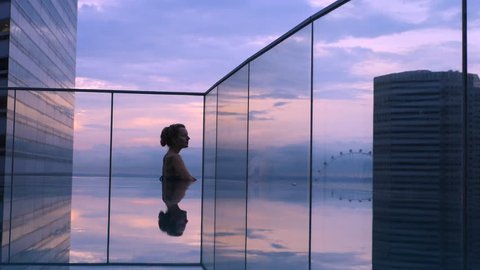 Woman Relaxing In Infinity Swimming Pool In Luxury Hotel At Sunset