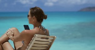attractive woman in teak chair with cellphone on a tropical beach
