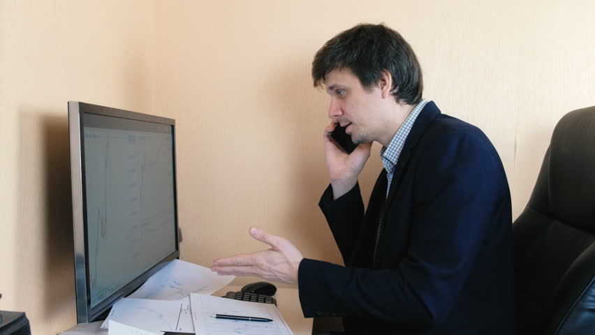 Frustrated man working at the computer and calling mobile phone. Compares graphics on the screen and on paper. | Shutterstock HD Video #1009256249
