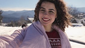 Happy curly woman make mobile selfie video at snowy mountain landscape
