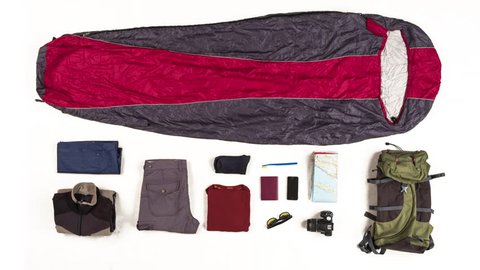 Top view on sleeping bag packing with travelers equipment on white background. 4k stop motion animation.