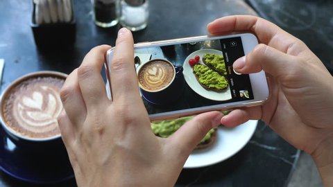 Female Hands Photographing Food For Breakfast By Smartphone. Coffee And Avocado Toast.