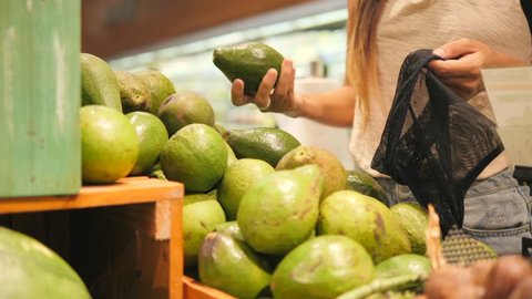 Vegan Zero Waste Girl Choosing Fresh Avocados in Supermarket. Young Mixed Race Woman Shopping without Plastic Bags in Grocery Store. 4K.