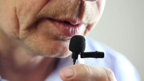 The man speaks into a small microphone in a low voice.
The lips of a man speak loudly in a whisper into a lapel microphone. Lavalier microphone