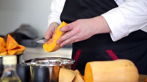 Professional chef is peeling juicy pumpkin. He is folding pumpkin seeds in a pot.