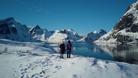 4k aerial drone footage - Women admiring the snow covered mountains of Reine, Norway.  Lofoten Islands archipelago.  