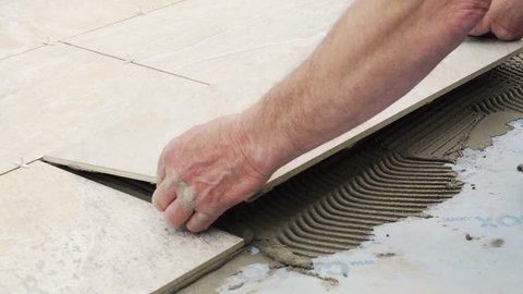A man places a tile on the floor on top of cement. The tile is of mineral colors, like slate.