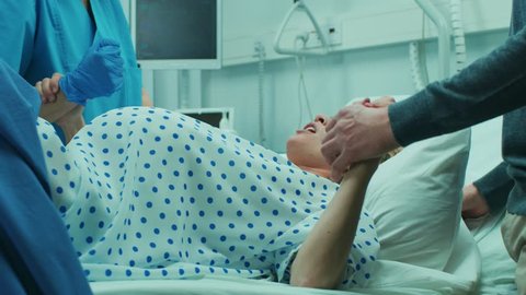 In the Hospital, Close-up on a Woman in Labor Pushing Hard to Give Birth, Obstetricians Assisting, Spouse Holds Her Hand. Modern Maternity Hospital with Professional Midwives. Shot on RED EPIC-W 8K.