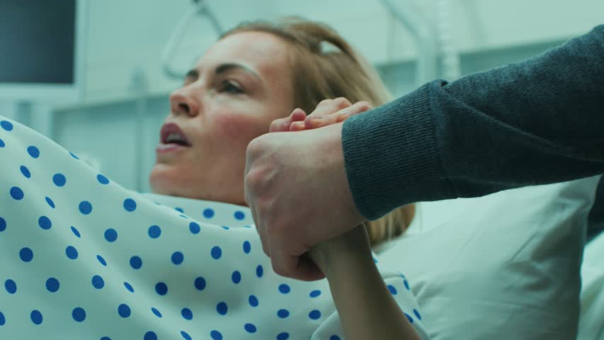 Close-up on a Face of a Woman in Labor Pushing Hard to Give Birth, Obstetricians Assisting, Spouse Holds Her Hand. Modern Maternity Hospital with Professional Midwives. Shot on RED EPIC-W 8K Camera. Royalty-Free Stock Footage #1009293506