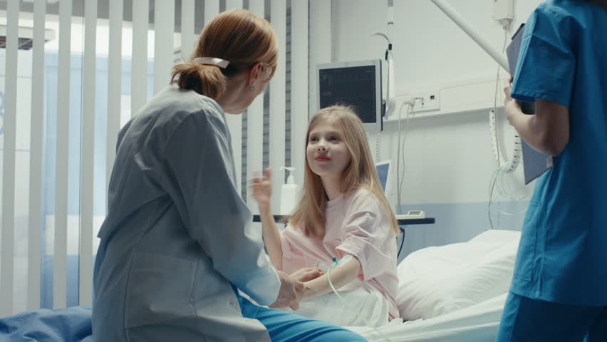 Cute Little Girl Sits on a Hospital Bed and Talks with Friendly Woman Doctor. Children's Hospital Pediatric Ward. Top Quality Health Care. Shot on RED EPIC-W 8K Helium Cinema Camera.