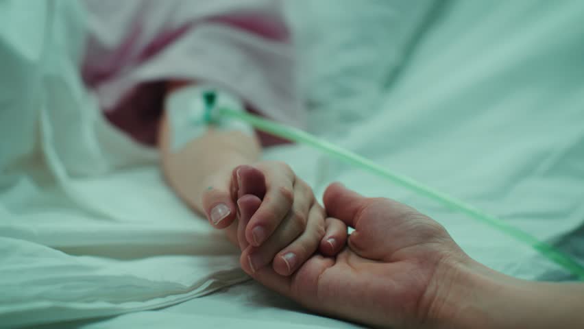 Recovering Little Child Lying in the Hospital Bed Sleeping, Mother Holds Her Hand Comforting. Focus on the Hands. Emotional Family Moment. Shot on RED EPIC-W 8K Helium Cinema Camera.