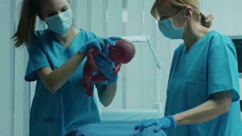 In the Hospital Woman in Labor Pushes and Gives Birth, Baby Comes out, Obstetricians Assist Delivery, Husband Supports His Wife. Side View Footage. Shot on RED EPIC-W 8K Helium Cinema Camera.