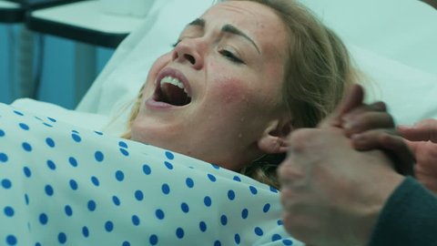 Close-up on a Face of a Woman in Labor Pushing Hard to Give Birth, Husband Holds Her Hand. Woman in Pain, Has Contractions. Shot on RED EPIC-W 8K Helium Cinema Camera.