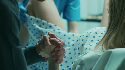 In the Hospital Woman Giving Birth, Husband Holds Her Hand in Support, Obstetricians Assisting. Modern Delivery Ward with Professional Midwives. Shot on RED EPIC-W 8K Helium Cinema Camera.