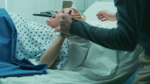In the Hospital Close-up on Woman in Labor Pushes to Give Birth, Obstetricians Assisting, Husband Holds Her Hand. Modern Delivery Ward with Professional Midwives. Shot on RED EPIC-W 8K Helium Camera.