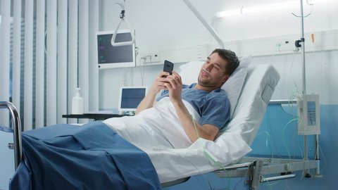 Recovering Patient Uses Smartphone while Lying on a Bed in the Hospital. Friendly Nurse Comes in to Check on Him. Shot on RED EPIC-W 8K Helium Cinema Camera.