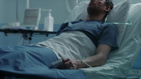 In the Hospital Sick Male Patient Sleeps on the Bed, Nurse Enters Medical Ward Checks His Vitals and Drop Counter. Sad and Blue Scene. Shot on RED EPIC-W 8K Helium Cinema Camera.
