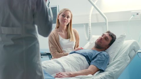 In the Hospital, Patient Lying in Bed, his Wife Sitting Beside, They Listen to Doctor's Explanations. Love and Care Concept. Shot on RED EPIC-W 8K Helium Cinema Camera.